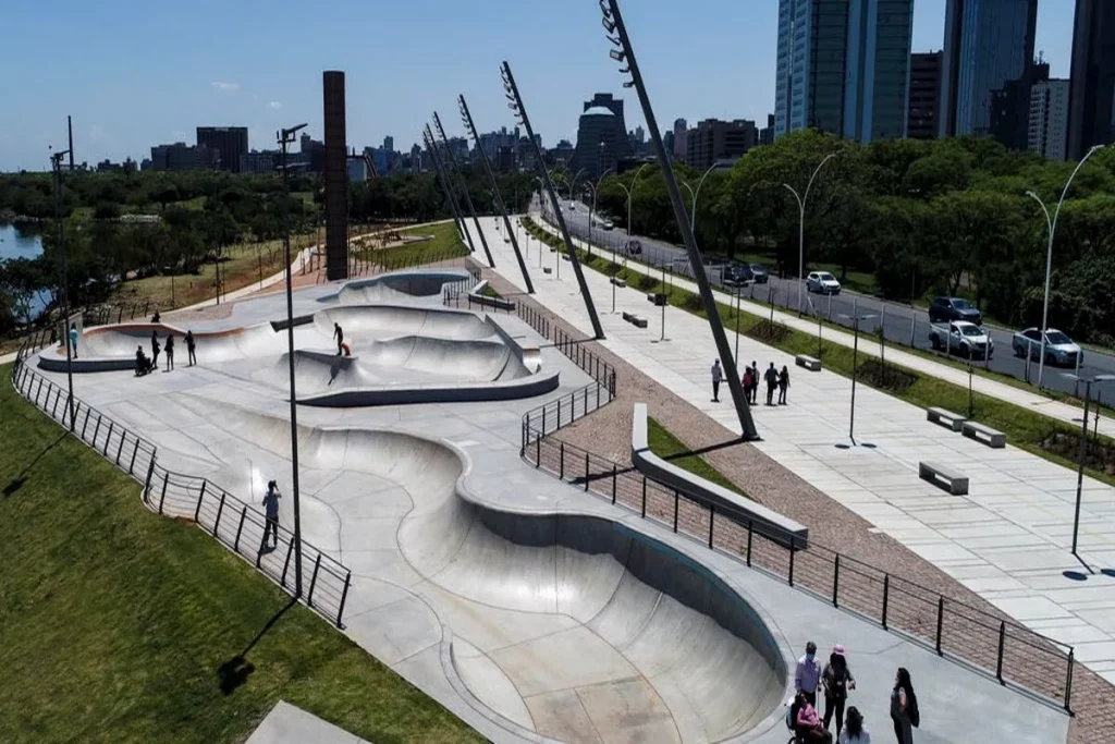 Pista de skate moderna em área urbana arborizada com pedestres e ciclistas ao redor