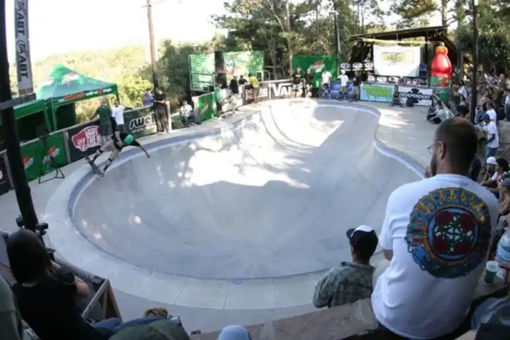 Skatista realizando manobra em pista bowl durante campeonato com público ao redor.