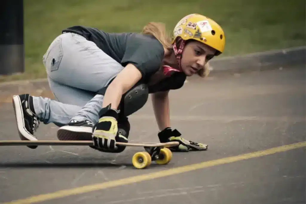 Mulher praticando longboard com capacete e luvas de proteção em pista asfaltada