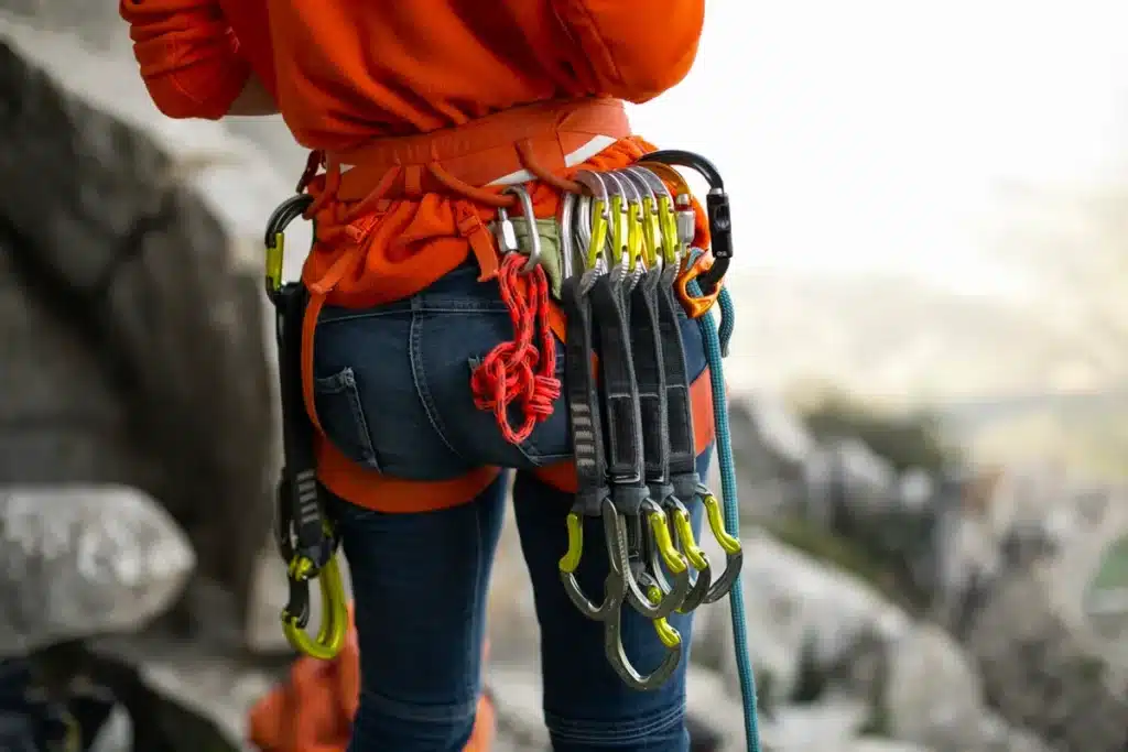 Escalador usando arnês e mosquetões coloridos, pronto para rapel em rocha, com cordas e equipamento pendurados