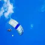 Pessoas realizando salto de paraquedas com céu azul ao fundo