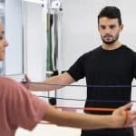 Pessoa fazendo exercício de propriocepção com elásticos na fisioterapia, acompanhada por um profissional.