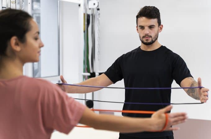 Pessoa fazendo exercício de propriocepção com elásticos na fisioterapia, acompanhada por um profissional.
