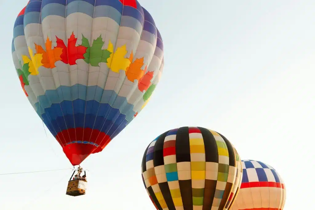 Imagem de balões de ar quente coloridos no céu, com um balão em destaque em tons de azul, vermelho e folhas coloridas.