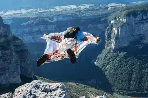 Pessoa usando traje wingsuit com estampa de tigres realizando salto de base jump de um penhasco alto, com cânion profundo e florestas ao fundo.