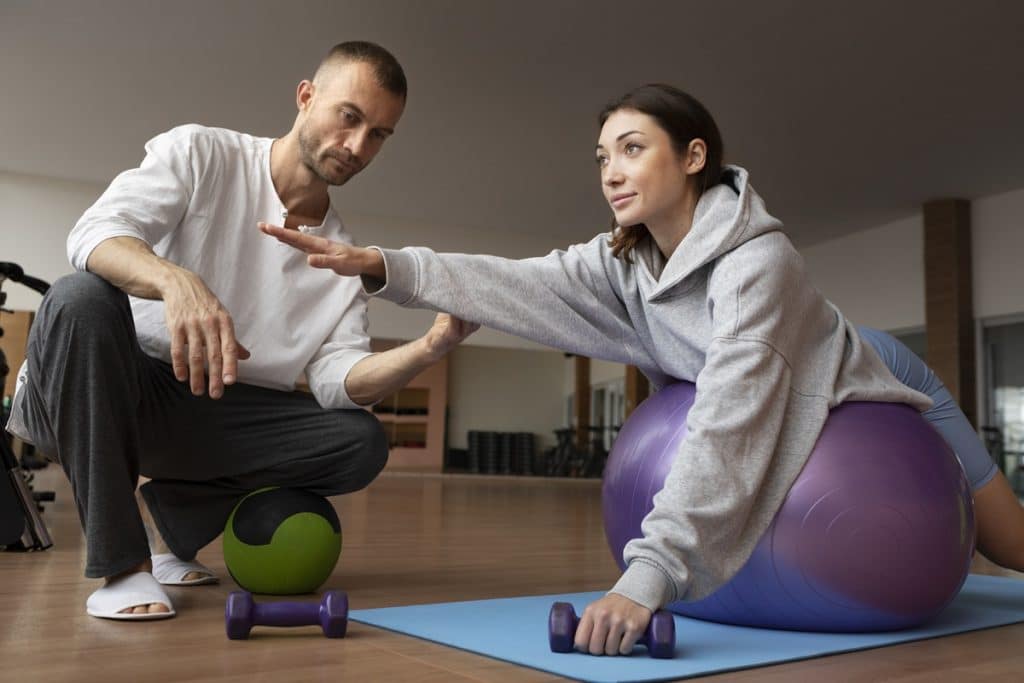 Mulher praticando exercício de propriocepção com bola suíça, sendo orientada por um fisioterapeuta.