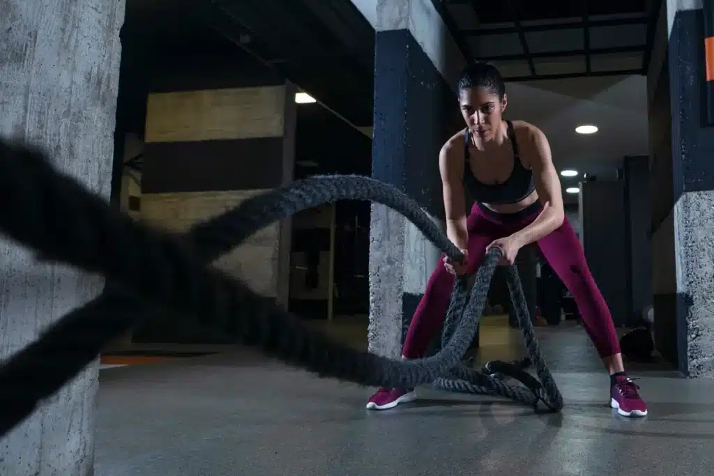 Mulher realizando exercício com corda naval em treino HIIT, focada e com roupas esportivas.