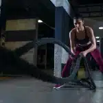 Mulher realizando exercício com corda naval em treino HIIT, focada e com roupas esportivas.