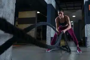 Mulher realizando exercício com corda naval em treino HIIT, focada e com roupas esportivas.