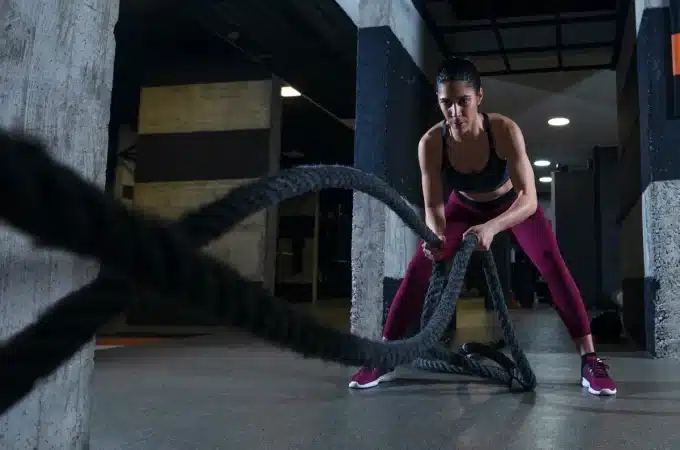 Mulher realizando exercício com corda naval em treino HIIT, focada e com roupas esportivas.
