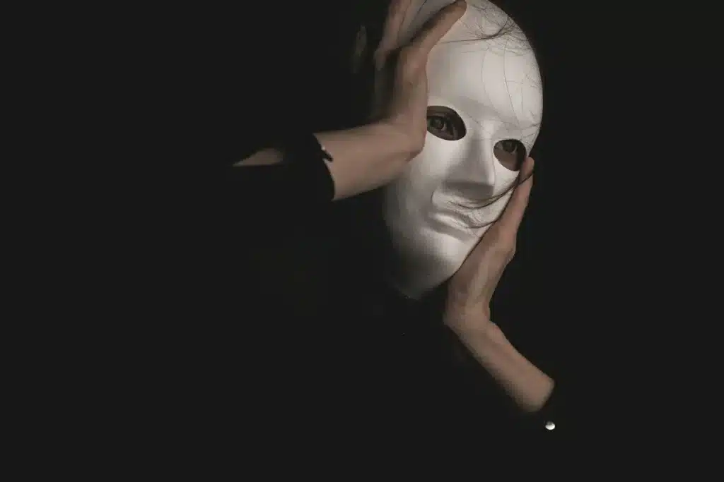 Pessoa segurando uma máscara branca no rosto, com olhos visíveis através das aberturas, simbolizando a síndrome do impostor