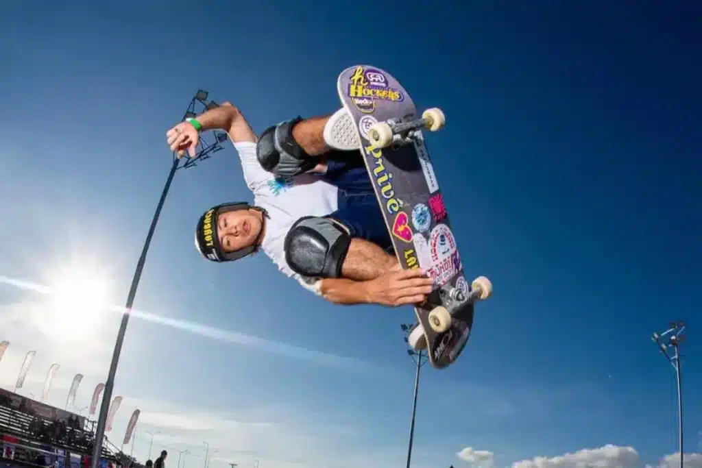 Skatista executando manobra aérea em competição de skate park com céu azul ao fundo.