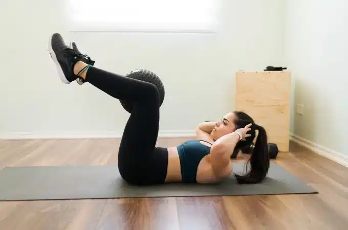 Mulher praticando exercícios de core usando bola suíça em um tapete de yoga, em uma sala de treino em casa
