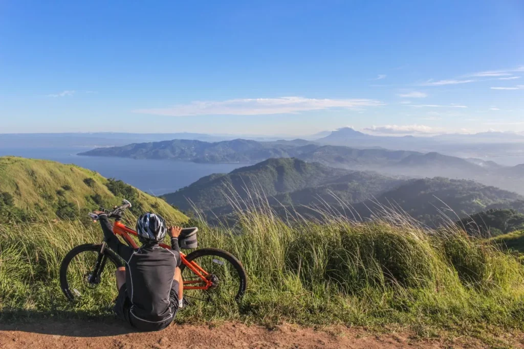 Ciclista de mountain bike sentado no topo de uma montanha, admirando a vista panorâmica de um lago e outras montanhas, representando a liberdade do MTB.