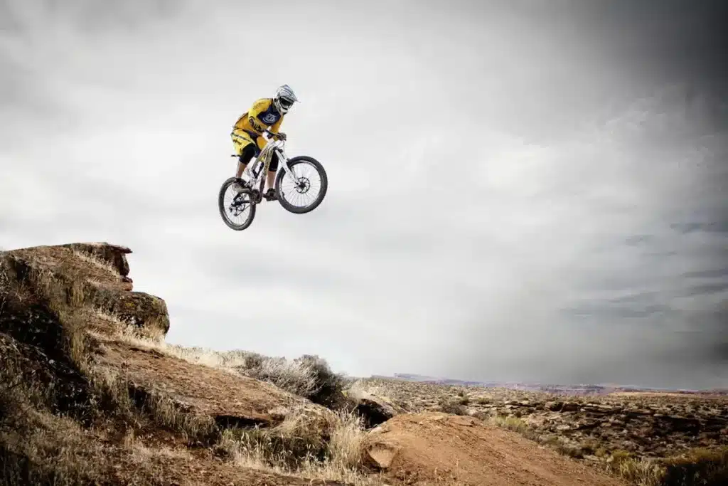 Ciclista de mountain bike realizando um salto espetacular no ar sobre uma paisagem rochosa e desértica, representando a emoção do MTB.
