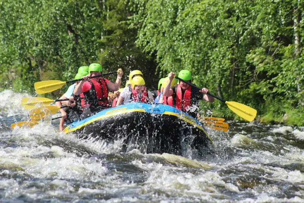 Grupo praticando rafting em bote inflável com remos amarelos em rio de corredeiras em Socorro SP, rodeado por mata verde.