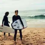 Duas pessoas na praia, cada uma com sua prancha de surf