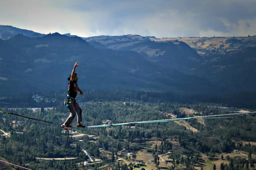 Pessoa praticando highline em corda suspensa sobre vale com montanhas e floresta ao fundo