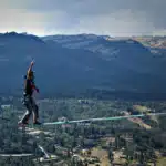 Pessoa praticando highline em corda suspensa sobre vale com montanhas e floresta ao fundo