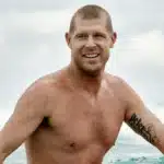 surfista dentro do mar olhando para o lado com expressão sorridente após sair de uma onda