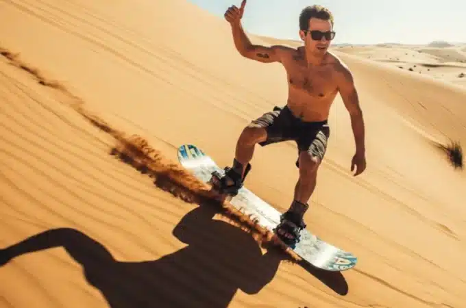 homem praticando sandboarding descendo duna de areia com prancha