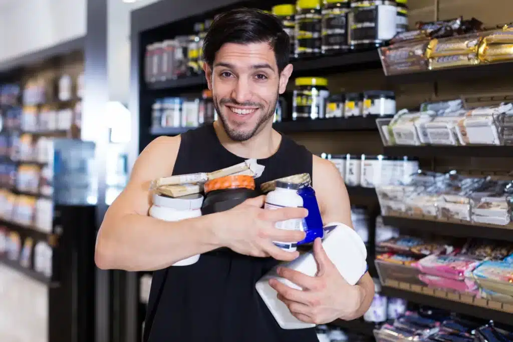 homem segurando diversos potes de suplementos em loja de nutrição esportiva