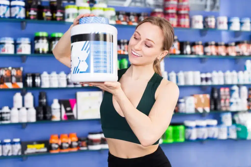 mulher segurando pote grande de suplemento proteico em loja de produtos fitness